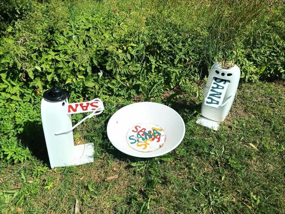 kaksi valkoista hahmoa ja keskellä laitanen jossa sanoja, hahmot syövät jotain metalliliuskaa jossa lukee sana