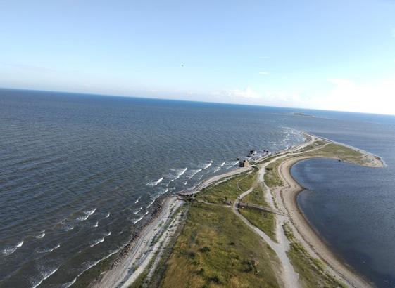 Una pequeña península verde con paradas de arena a cada lado que se adentran en el mar. La foto está tomada desde el faro de arriba.