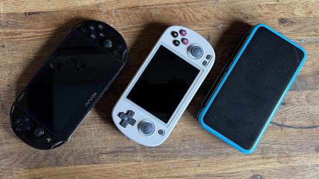 Handheld gaming devices lying on butcher block. PS Vita, Anbernic RG40XX-H, New Nintendo 2DS XL