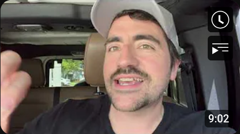 A white man in a baseball cap, talking in his car