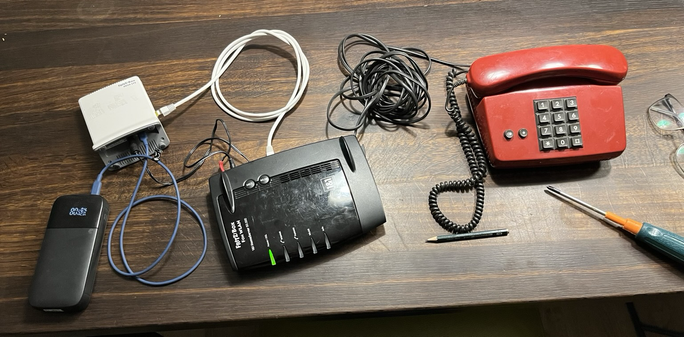 eine usb c powebank, die eine fritzbox 6820 lte mit strohm versorgt. diese ist wiederum mithilfe eines lan und hohlstecker kabel mit einer box 7390 verbunden, an welcher schliessendlich ein FeTAp 0172 Telefon der deutschen bundespost haengt.