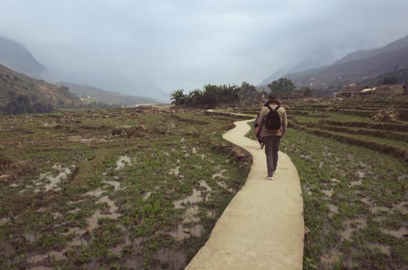 A man walking on a pathway through rice fields on a cloudy day somewhere in Vietnam