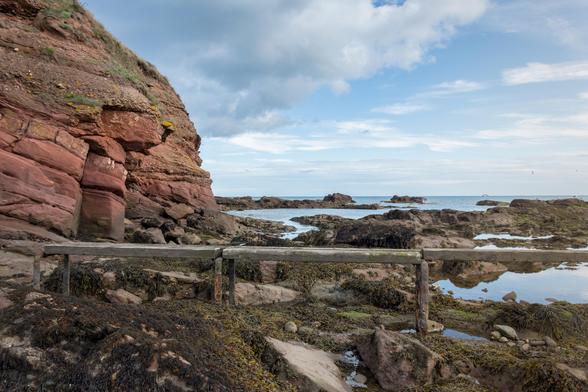 EN: On the left side of the picture, you can see the rugged cliffs, whose algae-covered stone outcrops are clearly visible at low tide. The stone arms extend towards the North Sea, which can be seen on the right side. The afternoon sun (not visible in the picture) makes the red sandstone shine particularly brightly.

DE: Auf der linken Bildseite ist die schroffe Steilküste zu sehen, deren algenbewachsenen Steinausläufer im Niedrigwasser der Ebbe gut zu sehen sind. Die steinernen Arme ragen zur Nordsee, die auf der rechten Seite zu sehen ist. Die etwas Nachmittagssonne (nicht im Bild) lässt den roten Sandstein besonders erstrahlen.