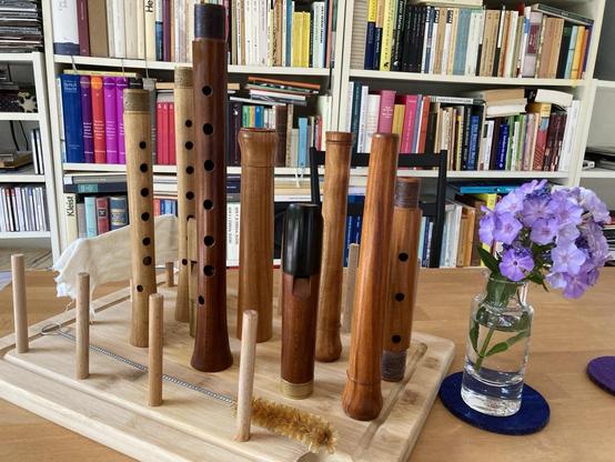 Photo of instrument joints (of early baroque recorders and a straight cornett) standing up on wooden board on which there is also a long hard brush and a small bottle of oil.