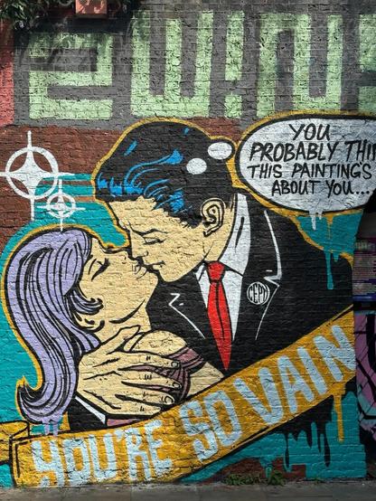 an aerosol art piece of a man and woman embracing, as in a comicbook panel. A caption says “you’re so vain”, and a thought bubble from the man reads “you probably think this painting’s about you”