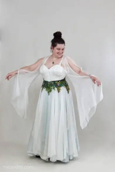 Photo d'une tenue de mariée blanche et verte, composée d'une longue jupe flottante aux reflets verts, d'un corset blanc et d'une ceinture verte pleinde feuilles et fleurs brodées ; des longues manches elfiques en voile sont attachées à des bretelles croisées.
