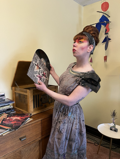 Wearing a vintage rickrack dress with dystopian augmentations, artist Klaire Lockheart slides a ZZ Top album from a record sleeve.