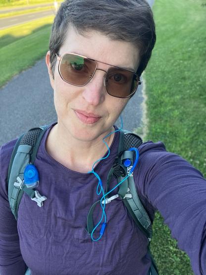 A selfie of a middle aged white woman mid run in sunglasses and a running pack.