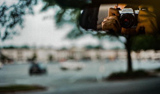 A photo of me taking a photo of me in the rear view mirror of my car with an early morning shopping center way out of focus in the main field of view.