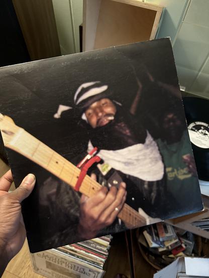 My hand holding a copy of Afelan by Mdou Moctar. The cover is a blurry closeup photo of him playing guitar and smoking a cig in traditional Tuareg attire.