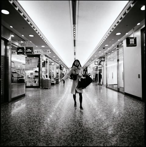 black and white photograph of a women walking towards the camera in a long shop lined parade.