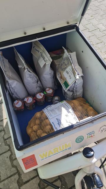Volles Lastenrad-Transportbox gefüllt mit Kartoffeln, Senf, Mehl, Haferflocken und Apfelsaft.
