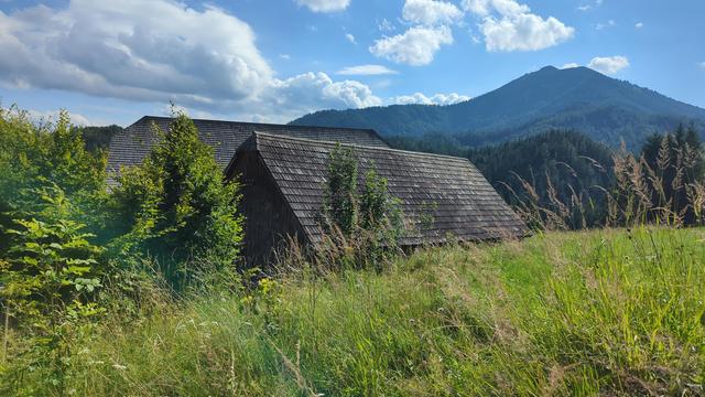 Holzschindeldach leicht verwittert, dahinter ein Berg vor blauem Himmel mit Wolken