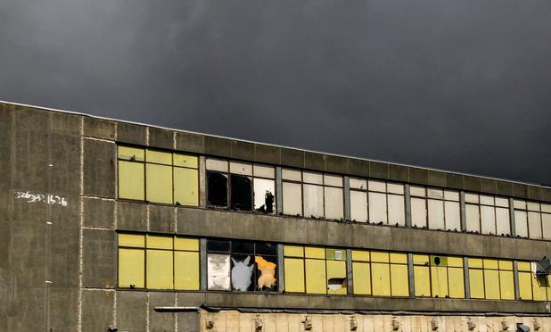 Angled view of a long wide decrepit abandoned office building with yellow window shades. The background above the building is an ominous black clouded sky.
