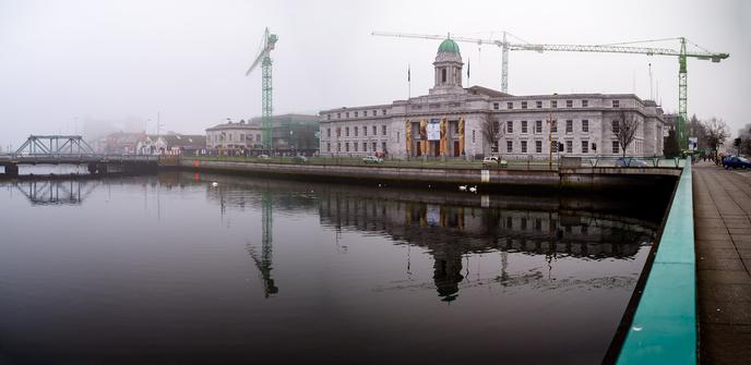 2005 photograph of Cork City Hall with its distinctive green dome reflected in the River Lee, showing construction cranes and the area before The Elysian development and modernisation, with swans visible on the calm water