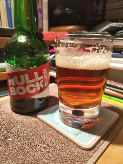 A bottle of the beer close to a small glass of it. Both on a small table with a bar towel.