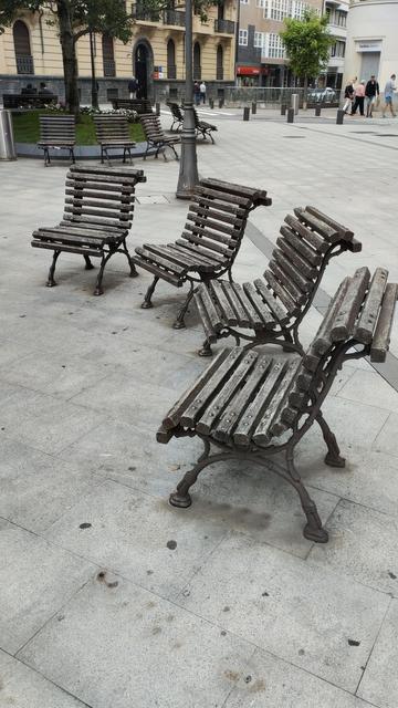 Foto urbana donde se ven cuatro mini bancos que están mirando al mismo punto y , más lejos, otros cuatro bancos dispuestos de tal forma que cada uno mira a un sitio diferente