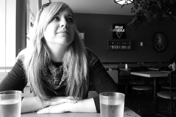 Portrait of a person in a bar, seated in front of drinks, er face highlighted by the beautiful light coming from the bay window on the left of the picture. The wall in the background features a row of beer bottles and a neon sign for the 'Belle Gueule' ('beautiful face') brewery. (Version françæ) Portrait d’æn personne dans æn bar, attablæ devant des consommations, læ visage mix en valeur par æn bæl lumière provenant dal baie vitræ à gauche de l’image. Sur læ mur à l’arrière-plan on voit æn rangée de bouteilles de bière et æn enseigne al néon dal brasserie 'Belle Gueule'.