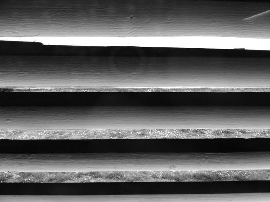 Close-up on the slats of a shutter. Outside the white light of a hot day. (Version françæ) Grox plan sur les lames d’æn volet avec læ lumière blank d’æn journée de canicule dehors.