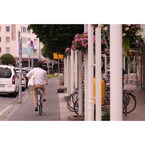 Fahrer und Fahrrad radeln neben den mit Blumen behängten Arkaden davon
