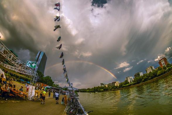 ein Regenbogen von einer Seite des meines hinüber zur EZB. Dramatischer Himmel. Eine Girlande zieht durch die Mitte des Bildes.