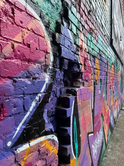 close-up of a wall covered with colourful aerosol art. There is a gap in a layer of bricks, which the art paints over.
