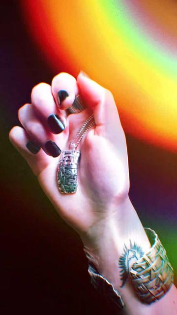 Hand holding a silver necklace, on the arm a bracelet also silver and in the background a rainbow