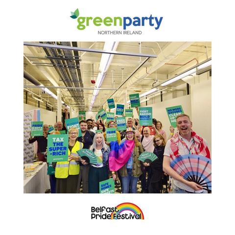 A joyful group of Green Party Northern Ireland members and supporters gather for a photo at their first Vegan Pride Brunch during Belfast Pride Festival 2025. They hold placards with bold slogans such as “Tax the Super-Rich,” “Pride Is Not a Photo Op,” “Fight Racism, Build Solidarity,” “Free Palestine Now,” and “Safe Homes, Safe Streets.” Some wear Pride flags and bright outfits, and several hold colourful fans. The image is framed with the Green Party Northern Ireland logo above and the Belfast Pride Festival rainbow logo below. The indoor venue features bright lighting and a welcoming, celebratory atmosphere.