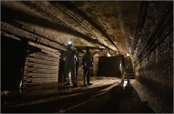 Trois égoutiers dans un collecteur. À gauche, des racks où sont entreposées plusieurs sections de batardeaux.