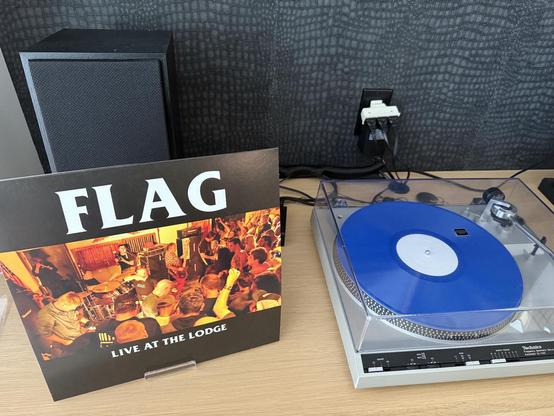 A picture of a record player with the Flag Live At The Lodge Album.

It’s a live tribute Album to Black Flag with
Bass-Chuck Dukowski
Drums-Bill Stevenson
Guitar-Stephen Egerton
Guitar/Vocals-Dez Cadena
Vocals-Keith Morris