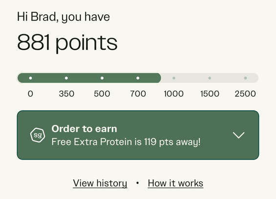 A progress bar in a restaurant app showing my progress toward rewards. The background is white. Black text at the top reads, Hi Brad, you have..." Beneath that in much larger black font, it reads "881." Immediately below, there is a progress bar with oval edges (a long horizontal rectangle with rounded corners). My points fill the shape with green, and white dots mark point delineations. The bar continued yes beyond my points as a gray bar with light green dots to mark important numbers. A green box beneath the progress bar reads, " Order to earn. Free Extra Protein is 119 points away!" There is a downward pointing arrow with two text options to view history and to see how it works. The interesting point to me is that the distance between dots on the progress bar is not constant. The markers on the progress bar represent 0, 350, 500, 700, 1000, 1500, and 2500. Ignoring the first jump from 0 to 300, that means the equal space between each pair of dots represents entirely different point values, from 150 to 1000, providing a false sense of progress toward the right (higher numbers).