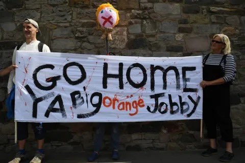 Protestors hold a sign that reads: "GO HOME YA Big orange Jobby"