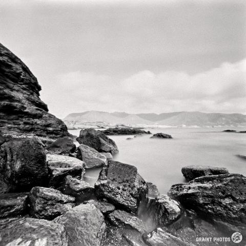 A black and white pinhole photograph of a rocky coastline by the sea