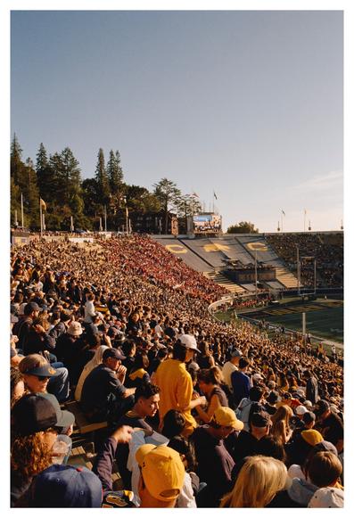 A sea of people in blue and gold outfit in the stands of Memorial Stadium, cheering for the California Golden Bears college football team. The end zone seating is tarped-off in blue with the UC Berkeley athletic logos and a banner saying “This is Bear Territory”. Near that section is a comparatively puny section of people in red, to see their Stanford Cardinals lose the game.