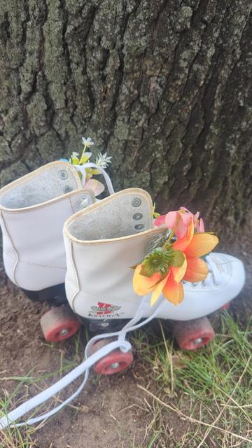 ein paar weisse Kinder Rollschuhstiefel mit roten Rollen steht an einem Baum. geschmückt mit künstlichen Blumen.