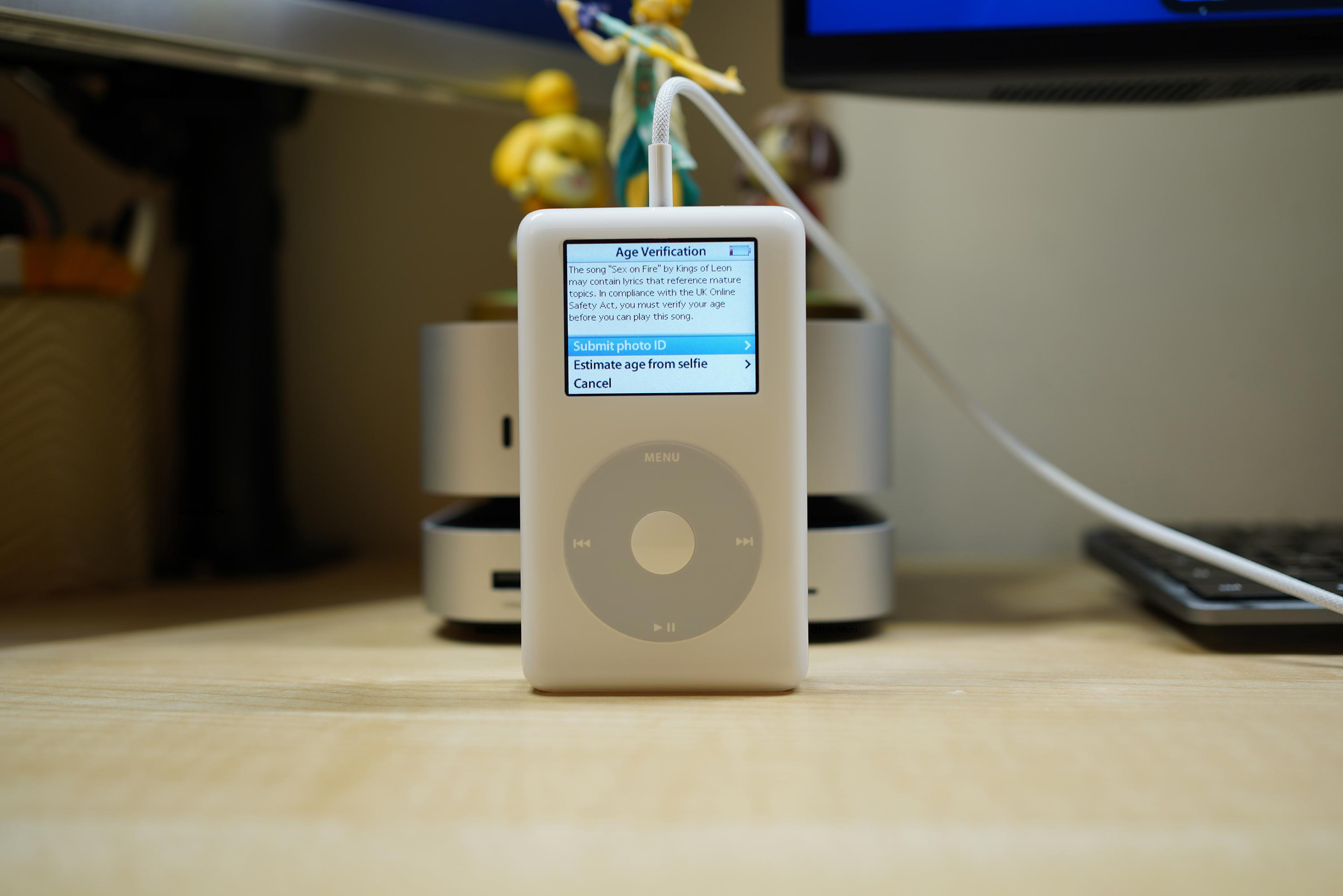 A 4th generation iPod displaying an error message that reads: The song "Sex on Fire" by Kings of Leon may contain lyrics that reference mature topics. In compliance with the UK Online Safety Act, you must verify your age before you can play this song. Three options are displayed: "Submit photo ID", "Estimate age from selfie", and "Cancel".