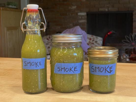 Homemade green jalapeno hot sauce in 3 separate jars on tabletop. Two are canning jars (12oz. and 16oz.) and one is a swing top w/red rubber seal.