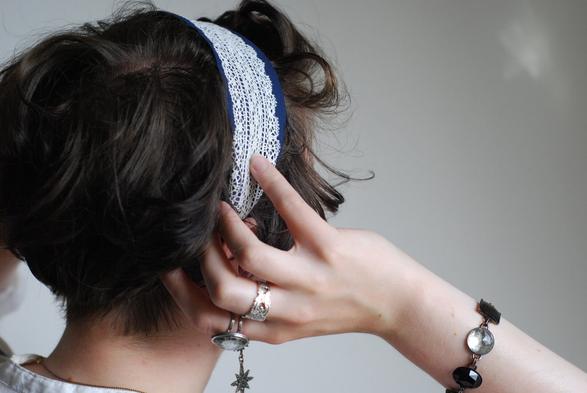 White woman with dark hair wearing a blue headband with a white lace sewn on it. Her back is to the camera and she is adjusting the strap around the ears