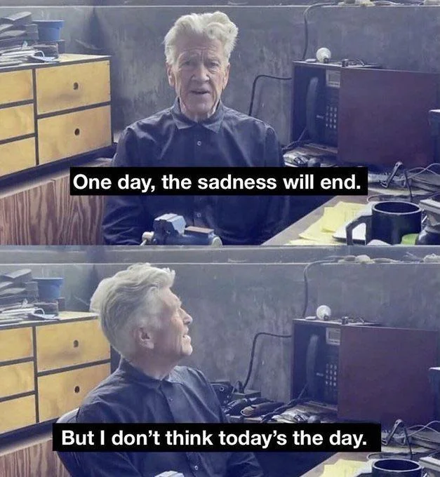 A two-panel meme features the  filmmaker David Lynch, a man with white hair, sitting at a desk with what appears to be a phone, and various desk items around him. The top panel shows Lynch looking forward, slightly upwards, with an open mouth as if speaking. A white text box overlays the image, stating: "One day, the sadness will end." The bottom panel shows Lynch looking upwards and to his right, with a more somber or reflective expression. Another white text box overlays this panel, stating: "But I don't think today's the day." The overall tone is melancholic with a touch of dark humor, characteristic of Lynch's artistic style, and the meme implies a prolonged state of sadness.