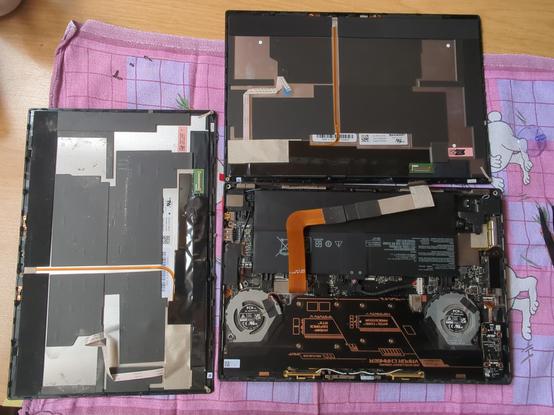 Opened laptop (tablet/convertible) with broken and new spare display on a table.