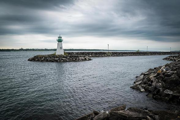 An old lighthouse stands on the rocky breakwater of the harbour in the small town of Prescott, Ontario on a gloomy day.