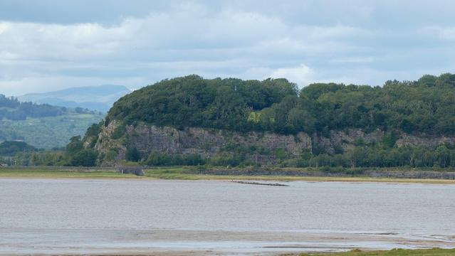 A view towards Meathop Fell, Westmorland, north western England. July 2025. This is taken from across the estuary of the River Kent which enters Morecambe Bay near the village of Arnside. The single track railway line at the base runs alongside the estuary. This railway line joins Lancaster to Barrow in Furness. In the background you can see another fell that is part of England's Lake District which is nearby.