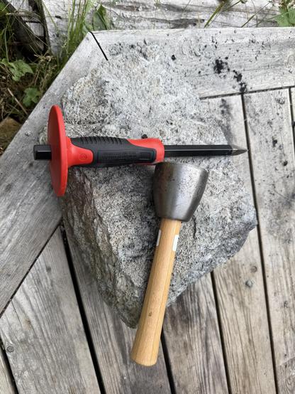 Photo of a hammer and chisel on top of a small stone.
