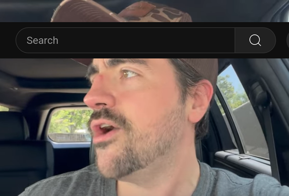 A white man in a baseball cap, talking in his car