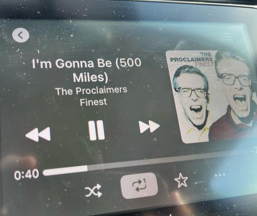 A car’s infotainment screen showing The Proclaimers I’m Gonna Be (500 Miles) is playing and 40 seconds have elapsed. The single song repeat indicator is on.