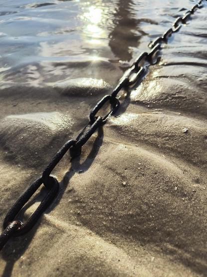 A rusty metal chain lies on the undulating sandy bottom of the North Sea beach at low tide. Indirect sunlight makes the damp sand shine.

Eine rostige Metallkette liegt auf dem gewellten Sandboden des Nordseestrandes bei Ebbe. Indirektes Sonnenlicht lässt den feuchten Sand strahlen.