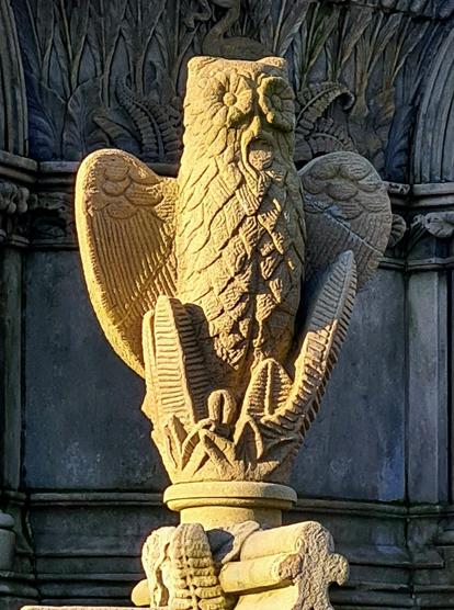 A sculpted owl, wings partially open with a worm or a small snake in its beak.