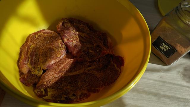 drei marinierte Scheiben Halsgrat liegen in einer gelben Schüssel, daneben ein Glas mit dem Schriftzug "Magic Dust"