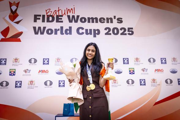Photo of Divya with her golden medal around her neck, trophy in left hand and flowers is right hand. In the background it says FIDE Women's World Cup 2025.
Photo by: Anna Shtourman.