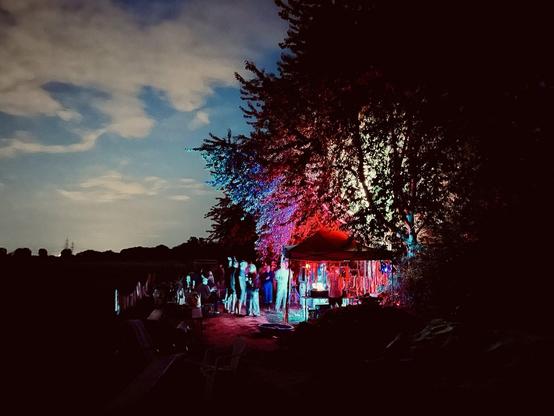 Bunt beleuchteter Pavillon mit vielen Menschen am Rande eines Feldes in der Abenddämmerung